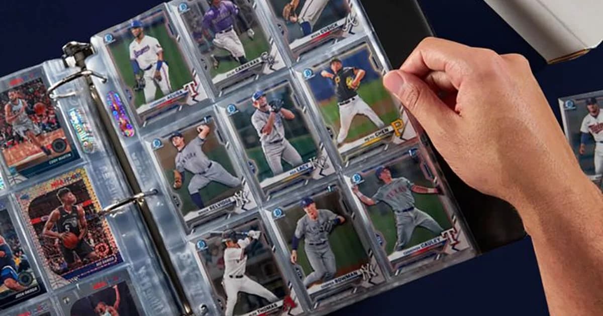 A hand turning a binder page of nine-pocket sheets filled with baseball cards, with basketball cards on the left page