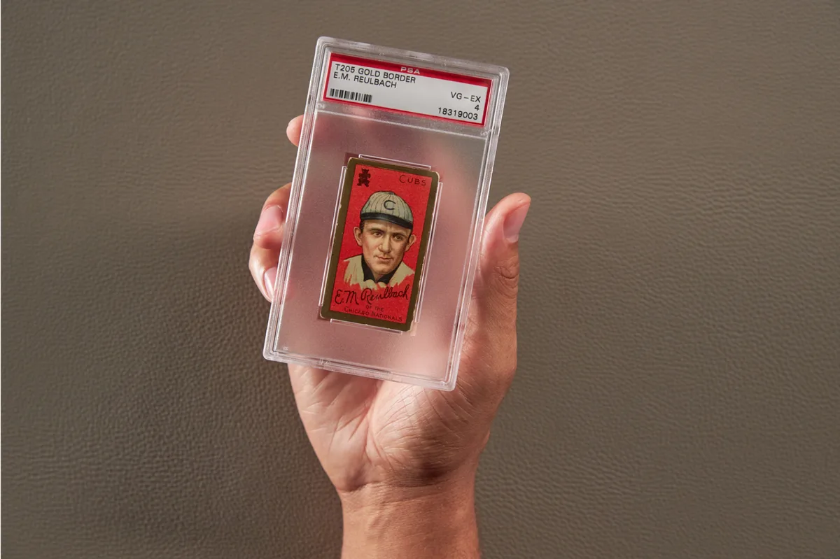 A hand holding a PSA slab of a T205 Gold Border E.M. Reulbach card graded VG-EX 4
