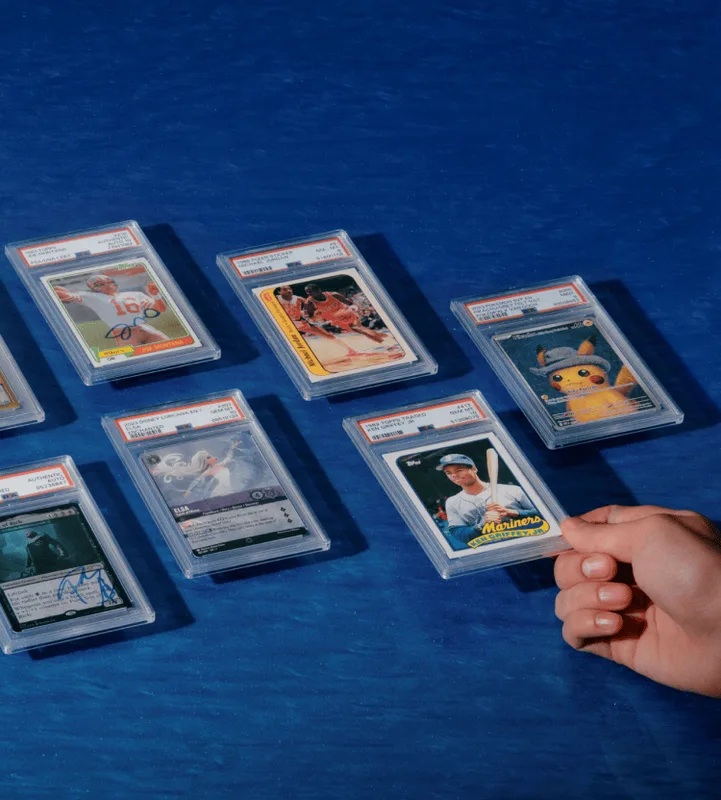 Graded card slabs spread on a blue background with a hand holding a slabbed Topps Mariners card, from eBay's trading card Authenticity Guarantee page