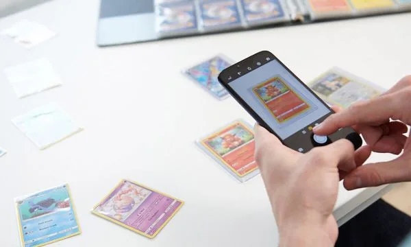 Hands photographing a trading card with a phone over a white table with several cards laid out, from eBay's seller guide